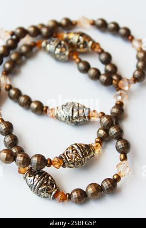Elegante handgefertigte Halskette aus braunen und bronzenen Perlen. Raffiniertes Bijoux aus nächster Nähe auf weißem Hintergrund. Damenmode, weibliches Accessoire. Stockfoto
