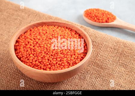 Rote Linsenkörner in einer Holzschale und Löffel auf einem Sackleinen. Draufsicht der getrockneten orangen Linsen in der Schüssel. Stockfoto