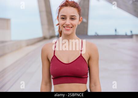 Lächelnde athletische Frau in Sportswear im Freien im urbanen Setting Stockfoto