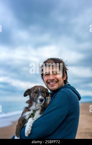 Mann, der einen braunen Hund auf dem Schoß hält, lächelnd und ich Stockfoto