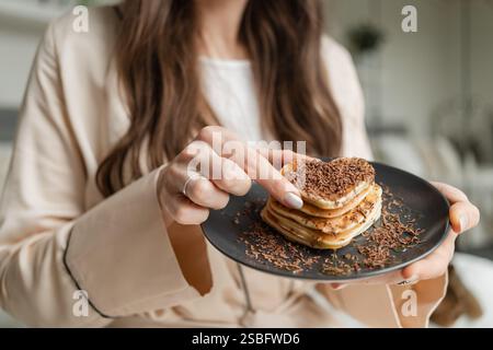 Frau, die herzförmige Pfannkuchen mit geriebener Schokolade zum Frühstück probiert hat Stockfoto