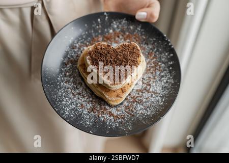 Handplatte mit herzförmigen Pfannkuchen mit geriebener Schokolade Stockfoto