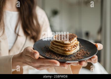 Frau, die Teller mit herzförmigen Pfannkuchen mit geriebener Schokolade hält Stockfoto