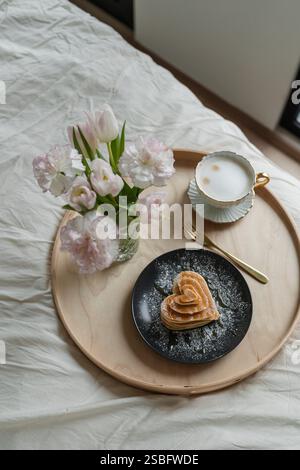 Überraschungsfrühstück im Bett mit herzförmigen Pfannkuchen und Kaffee Stockfoto