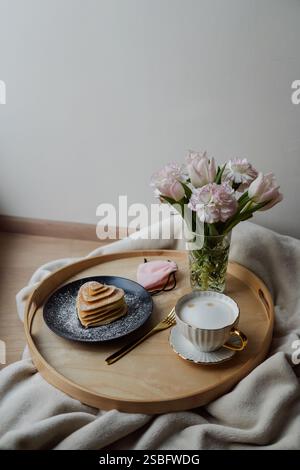 Herzförmige Pfannkuchen auf Tablett mit Kaffeetasse, Blumen und Geschenk Stockfoto