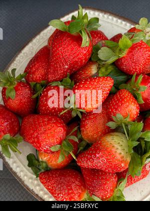 Diese Nahaufnahme zeigt einen Teller voller frischer, saftiger Erdbeeren. Die kräftigen roten Farbtöne der Erdbeeren bilden einen schönen Kontrast zu ihren Stockfoto