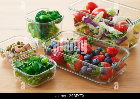 Gesunde vegane Lebensmittelzubereitungen für eine Woche in Glasbehältern auf Holztisch. Gemüse, Nüsse, Beeren in Kisten. Stockfoto
