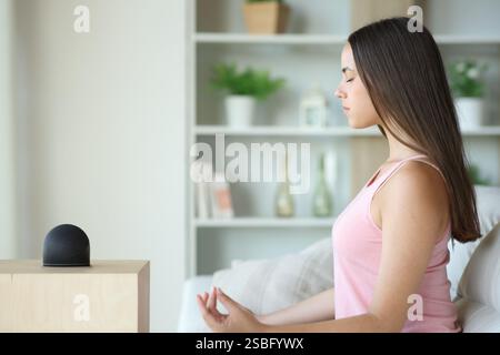 Frau, die Yoga macht, mit intelligentem Lautsprecher, die zu Hause auf einer Couch sitzt Stockfoto