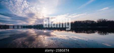 Eine atemberaubend friedliche Sonnenuntergangsszene über einem ruhigen, ruhigen See mit wunderschönen Reflexen der leuchtenden Farben am Himmel und einer dramatischen, wirbelnden Wolkenlandschaft voller verschiedener Wolken Stockfoto