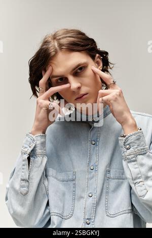 Ein hübscher junger Mann in Denim-Hemd zeigt eine nachdenkliche Pose vor einem gedämpften Hintergrund. Stockfoto