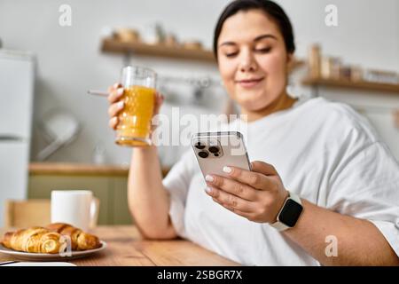 Eine junge Frau in Übergröße entspannt sich in einem rustikalen Café, schlürft einen Drink und scrollt auf ihrem Smartphone. Stockfoto