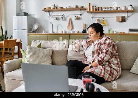 Die junge Frau in Übergröße sitzt bequem auf der Couch, in einem warmen Raum mit ihrem Telefon. Stockfoto