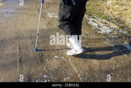 Alter Mann mit Gehhilfe im Winter auf schwarzem Eis, Rutschgefahr Stockfoto