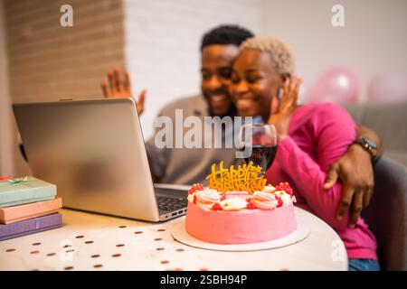 Glückliches junges Paar, das zu Hause den Geburtstag der Frau feiert. Sie haben Videoanrufe mit der Familie. Stockfoto