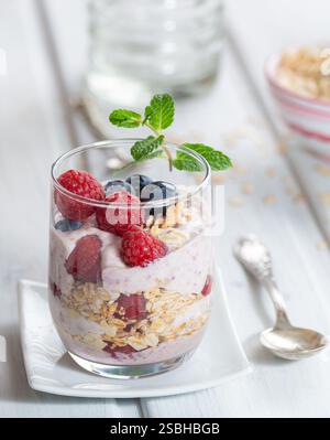 Gesundes Dessert - Himbeeren und Heidelbeeren mit Joghurt und Müsli in einem Glas auf weiß Stockfoto