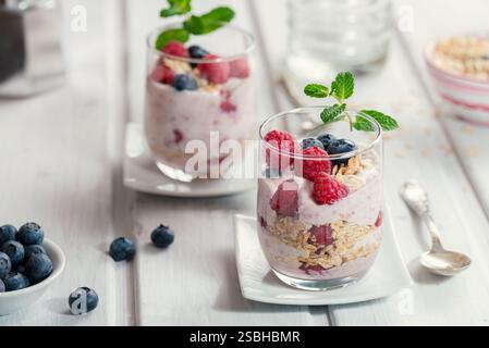 Gesundes Müsli - Himbeeren und Heidelbeeren mit Joghurt in Gläsern auf einem weißen Holztisch Stockfoto