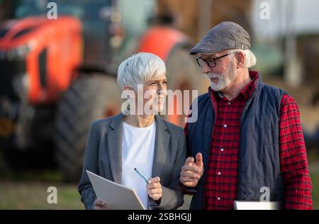Senior Bäuerin und reife Geschäftsfrau reden auf der Ranch vor dem Traktor Stockfoto
