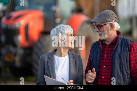 Senior Bäuerin und reife Geschäftsfrau reden auf der Ranch vor dem Traktor Stockfoto