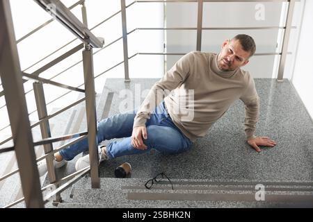 Verwundeter Mann auf Treppen im Gebäude nach dem Sturz. Gefährlicher Unfall Stockfoto