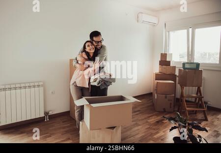 Glückliches Paar, das Kisten auspackt und umarmt und zusammen in ein neues Zuhause zieht Stockfoto