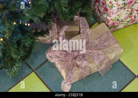 Wunderschön gewickelte Weihnachtsgeschenke, die mit bunten Bändern verziert sind, werden unter einem atemberaubenden Weihnachtsbaum platziert, der mit funkelnden blauen Lichtern geschmückt ist Stockfoto