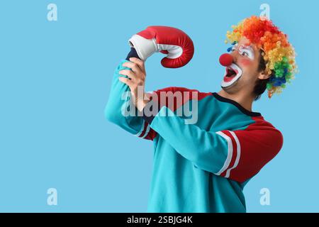 Porträt eines überraschten Clowns mit Boxhandschuh auf blauem Hintergrund. Aprilfeier zum Narrentag Stockfoto