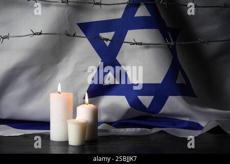Brennende Kerzen mit Stacheldraht und großer Flagge Israels auf dunklem Hintergrund. Holocaust-Gedenktag Stockfoto