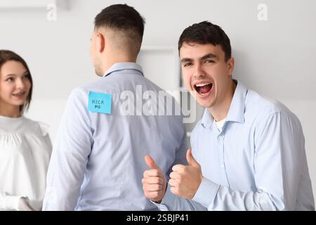 Junge Kollegen und Mann mit klebrigem Papier auf dem Rücken im Büro. Aprilfeier Stockfoto