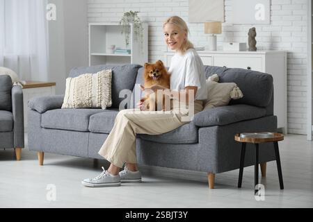 Reife Frau füttert süßen Pommerschen Hund auf Sofa zu Hause Stockfoto
