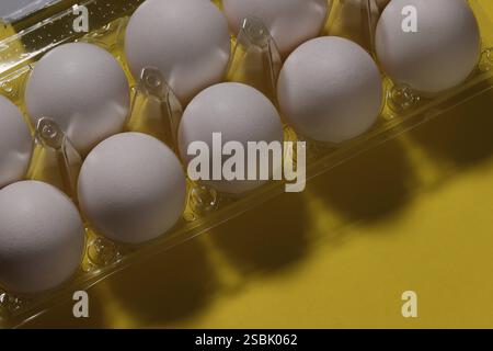 Nahaufnahme weißer Hühnereier in Kunststoffverpackung auf gelbem Hintergrund. Stockfoto