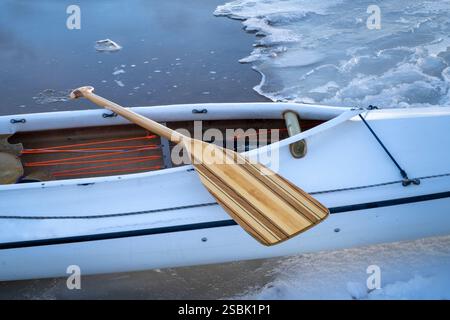 Gedecktes Expeditionskanu mit einem Holzpaddel an einem eisigen Seeufer Stockfoto