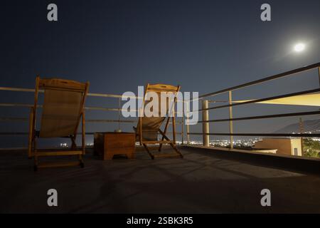 Leere Sonnenliegen und ein kleiner Holztisch auf der Dachterrasse mit Metallgeländer mit Blick auf die Stadt Stockfoto