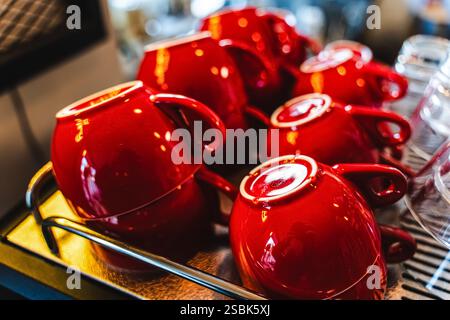 Viele rote Keramikkkaffeetassen auf einem Kaffeeautomatenregal in einem Café. Selektiver Fokus. Rote Kaffeetassen auf einem Regal in einem Café, zweite Reihe selektiver roter C Stockfoto