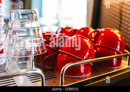 Viele rote Keramikkkaffeetassen auf einem Kaffeeautomatenregal in einem Café. Selektiver Fokus. Rote Kaffeetassen auf einem Regal in einem Café, zweite Reihe selektiver roter C Stockfoto
