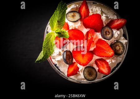 Erdbeeren mit Schlagsahne und Hüttenkäse, Minze und Heidelbeeren. Dessert in einem Glas auf einem schwarzen Glimmerbrett. Kopieren Sie einen Bereich. Hohe Qualität p Stockfoto