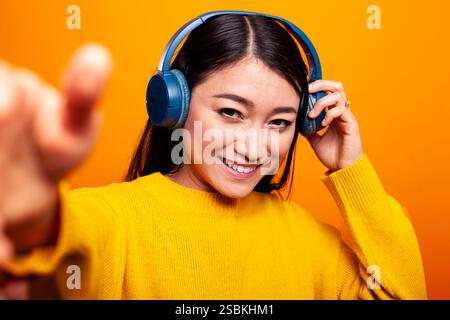 Lächelnde Frau, die die Kamera hält und ein Video aufnimmt, zeigt Enthusiasmus und Engagement. Fröhliche weibliche Vloggerin mit schnurlosen Kopfhörern, die einen pov-Livestream vor einem isolierten Hintergrund filmt. Stockfoto