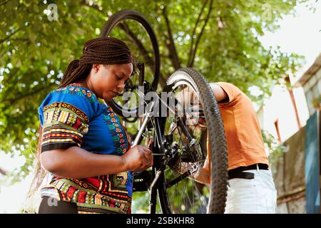 Junges und sportliches multiethnisches Paar, das Fahrradschäden mit professioneller Ausrüstung im Heim repariert. Gesund motivierter kaukasischer Mann und afroamerikanerin verwendet Werkzeuge, um defekte Fahrradkomponenten zu reparieren. Stockfoto