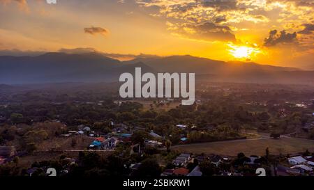 Golden Hour Sonnenlicht in einem malerischen Tal und Häuser eingebettet zwischen Bäumen und Feldern, schaffen eine ruhige und idyllische Szene in Mae Rim bei Chia Stockfoto