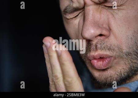 Schlechter Atem aus dem Mund. Nahaufnahme eines Mannes, der seinen Atem überprüft, indem er in seine Hand ausatmet, und zeigt Bedenken über Mundhygiene oder schlechten Atem Stockfoto