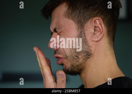 Schlechter Atem aus dem Mund. Nahaufnahme eines Mannes, der seinen Atem überprüft, indem er in seine Hand ausatmet, und zeigt Bedenken über Mundhygiene oder schlechten Atem Stockfoto