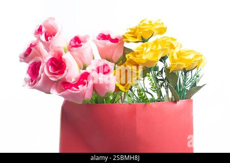 Farbenfrohes Arrangement mit rosafarbenen und gelben Rosenblüten in einem leuchtend roten Behälter, ideal für Dekoration oder Geschenke, Liebe und Freude. Stockfoto