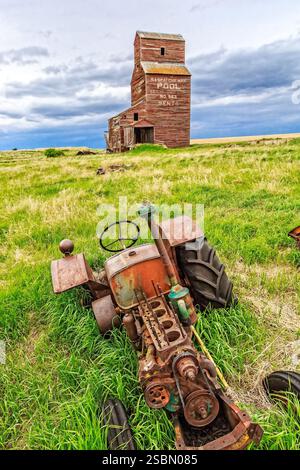 Ein alter, verrosteter Traktor steht auf einem Feld neben einem Getreidesilo. Der Traktor wird wahrscheinlich verlassen und rostet im Gras. sil Stockfoto
