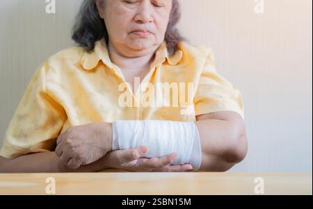 Alte asiatische Frau mit bandagiertem Arm, verletztem schmerzhaften Arm, sie sah es mit Sorge an. Selektiver Fokus. Stockfoto