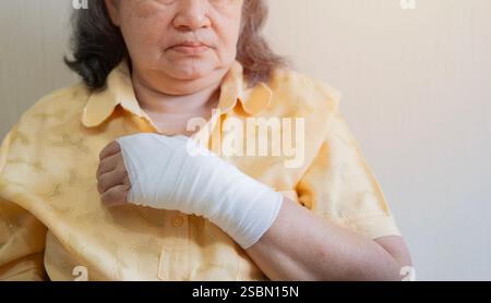 Alte asiatische Frau mit Mullverband um ihre verletzte Hand gewickelt. Erste Hilfe, Armbehandlung nach Verletzung. Stockfoto