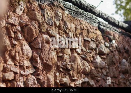 Eine Steinmauer aus Steinen verschiedener Größe und in rotbraunem Farbton gefärbt. Stockfoto