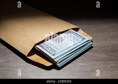 Ein Nahbild eines braunen Umschlags, gefüllt mit $100-Scheinen, auf einem Holztisch. Bestechungskonzept. Stockfoto