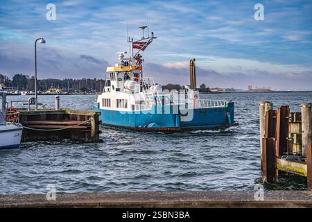 Eine farbenfrohe Fähre nähert sich einem Dock unter einem teilweise bewölkten Himmel und zeigt die friedliche Hafenlandschaft mit Wasserreflektionen, verankerten Booten und vibra Stockfoto