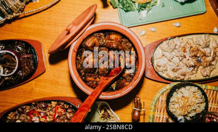 Ein Tisch mit einer Vielzahl von Speisen, einschließlich eines großen Topfes mit Essen in der Mitte. Der Tisch ist mit Schüsseln, Löffeln und anderen Utensilien besetzt. Die Szene ist erlebnisreich Stockfoto
