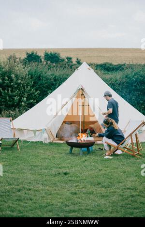 Ein Mann und eine Frau sitzen in einem Tipi mit einem Feuer in der Mitte. Das Tipi ist von Stühlen und einer Feuerstelle umgeben. Die Szene ist gemütlich und intim Stockfoto