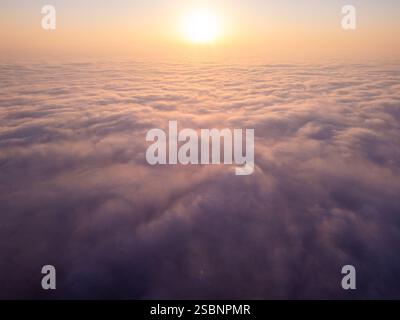 Ein atemberaubender Blick aus der Luft auf den Sonnenaufgang über einem riesigen Wolkenmeer. Das goldene Licht wirft ein sanftes Leuchten über den rollenden Nebel und erzeugt eine traumhafte, ruhige Atmosphäre Stockfoto